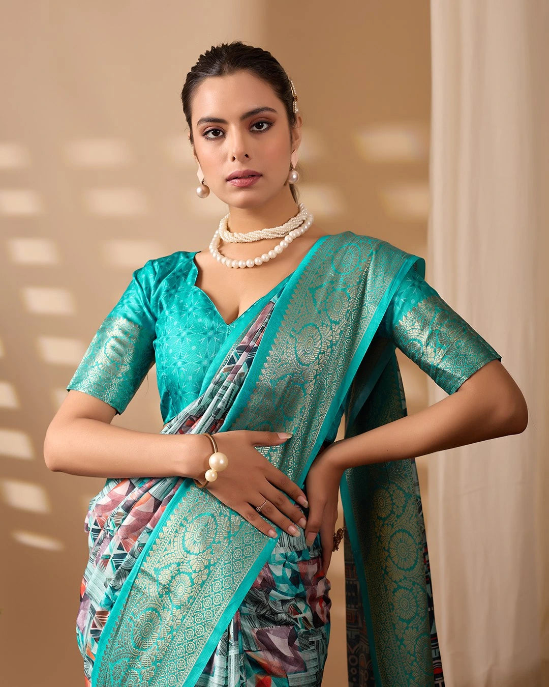 Woman wearing a teal saree with a patterned blouse against a beige background